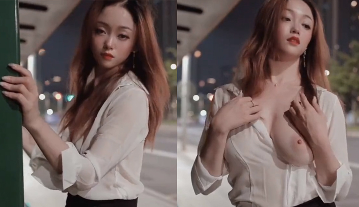 A gorgeous woman with a striking contrast, revealing her huge breasts in a beautiful scene next to a bus stop.